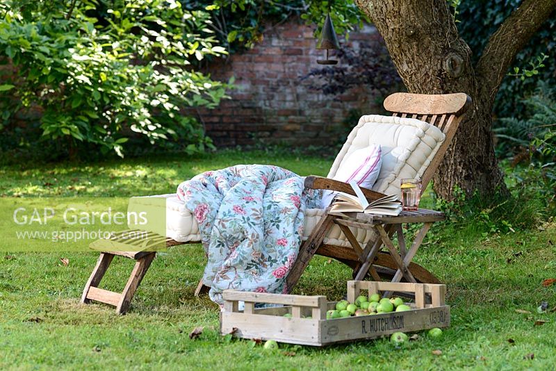 Transat en bois avec coussins et couverture sur une pelouse à l'ombre sous un arbre