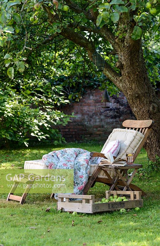 Transat en bois avec coussins et couverture sur une pelouse à l'ombre sous un arbre