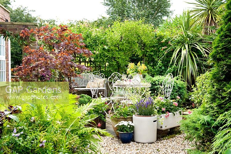 Petit jardin de gravier et pots et meubles blancs décoratifs entourés de treillis avec des grimpeurs pour plus d'intimité