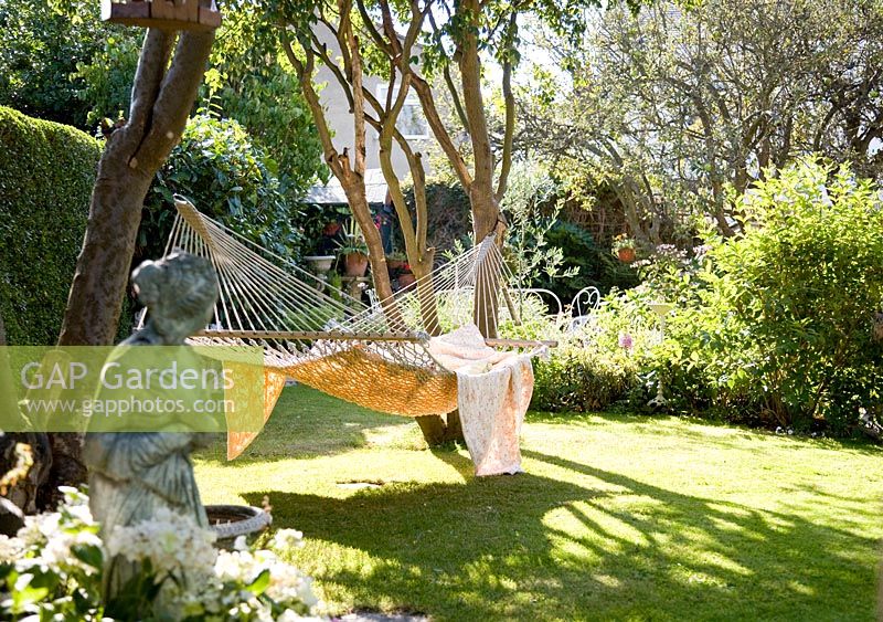 Grand hamac avec des couvertures accroché entre les arbres dans le jardin, sculpture en premier plan