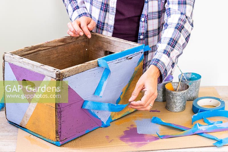 Woman remove masking tape pour révéler une boîte en bois peinte dans un motif géométrique multicolore
