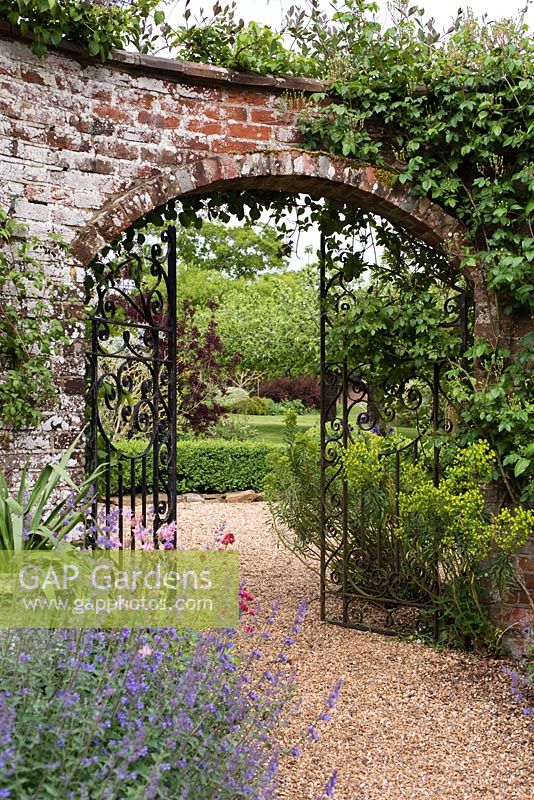 Une arche fermée en fer forgé dans un mur de manivelle serpentine ou froissée avec vue sur un jardin au-delà