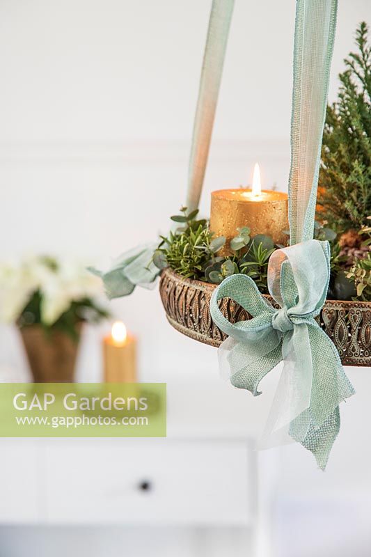 Détail de l'arrangement de l'Avent suspendu avec des bougies en or, arbre de Noël miniature et feuillage d'eucalyptus et de Hebe