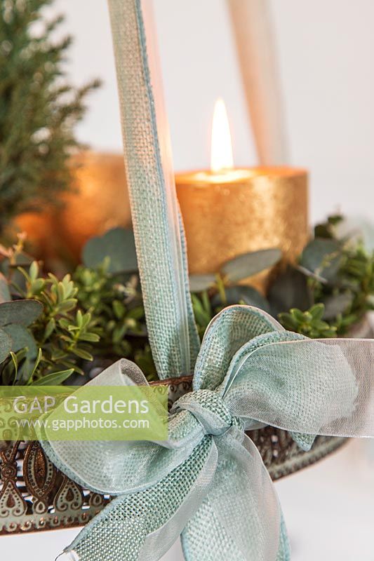 Détail de l'arrangement de l'Avent suspendu avec des bougies d'or, arbre de Noël miniature, eucalyptus et feuillage Hebe