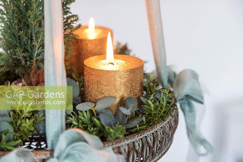 Détail de l'arrangement de l'Avent suspendu avec bougies en or, sapin de Noël miniature et feuillage d'eucalyptus et de Hebe.