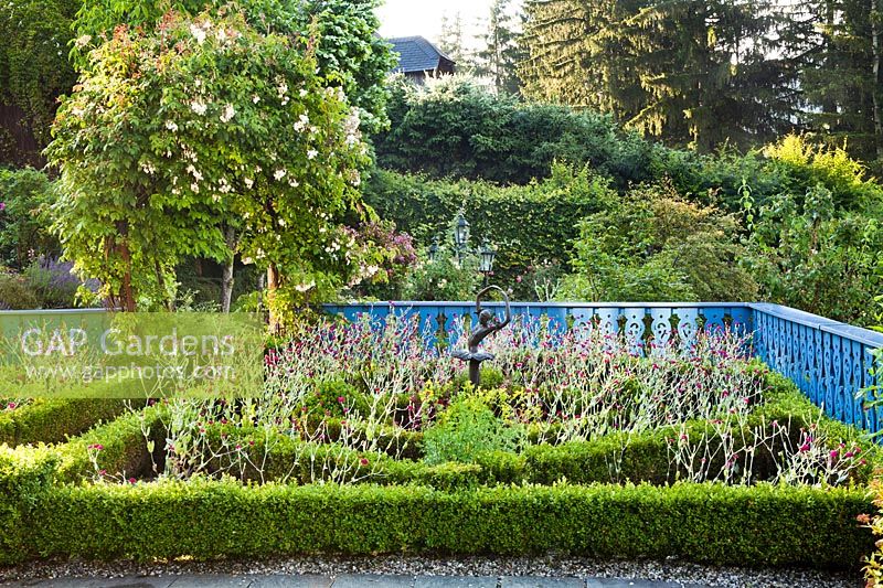 Jardin de noeuds avec statue et clôture bleue.