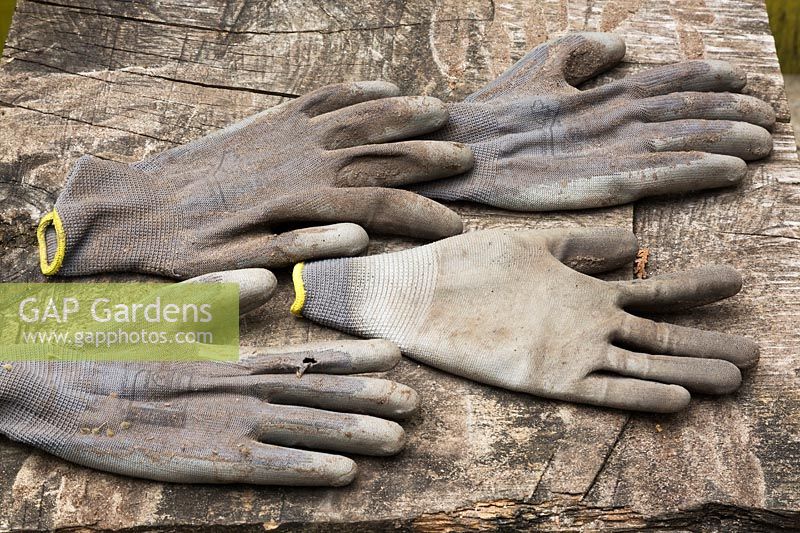 Gants de travail de jardinage en coton et caoutchouc gris usés sur une surface en bois