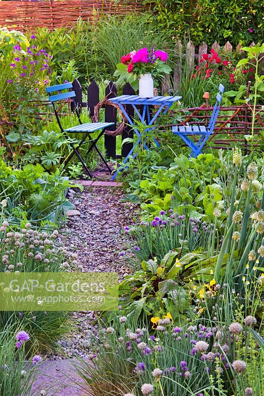 Table et chaises bleues installées dans un potager et des herbes aromatiques clos.