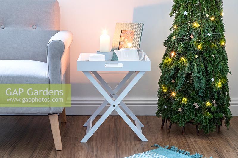 Sapin de Noël peu encombrant en pin - Abies et conifères - Feuillage de Juniperus attaché à un obélisque de saule et décoré de décorations et de lumières en étoile dans un salon moderne avec chaise et table d'appoint