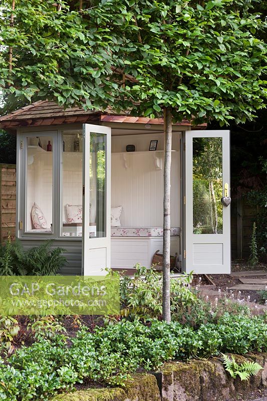 Une maison de jardin en bois hexagonale peinte gris pâle et crème sous les arbres de charme pleached - Juillet, Cheshire