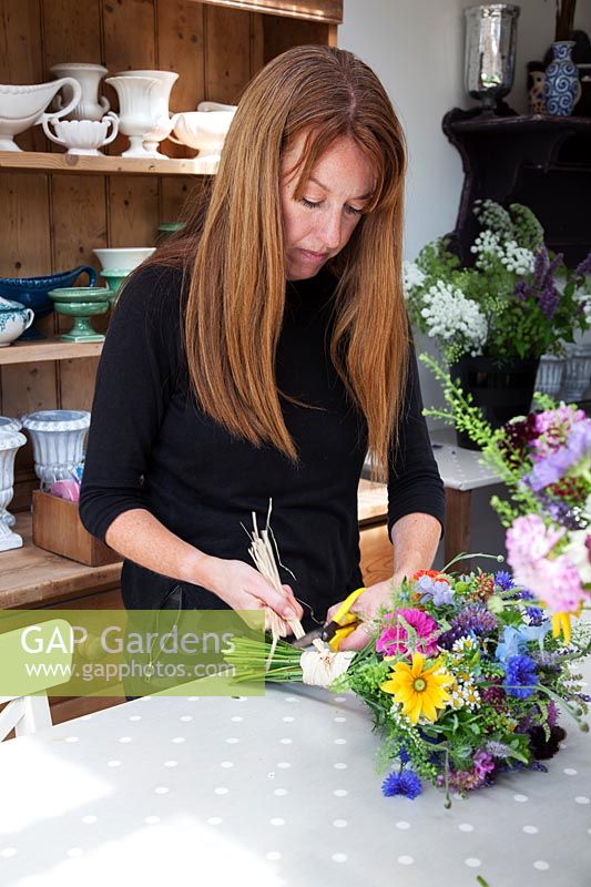 Zelie dans l'atelier de fleurs fabriquant des bouquets de fleurs attachés à la main et les fixant avec du raphia.