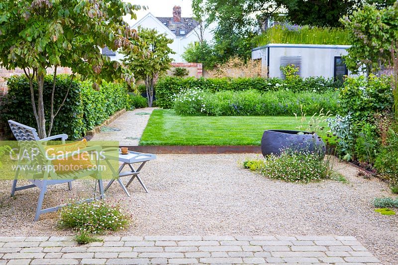 Un jardin de ville contemporain avec coin salon gravillonné, pelouse surélevée, parterre de fleurs sauvages et jardin au toit vert.