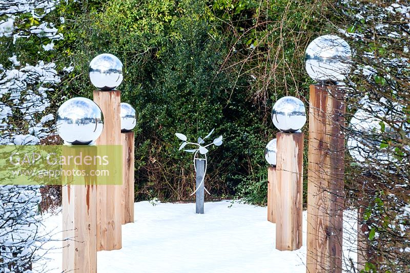Avenue de poteaux en bois surmontés de globes en acier inoxydable dans la neige.