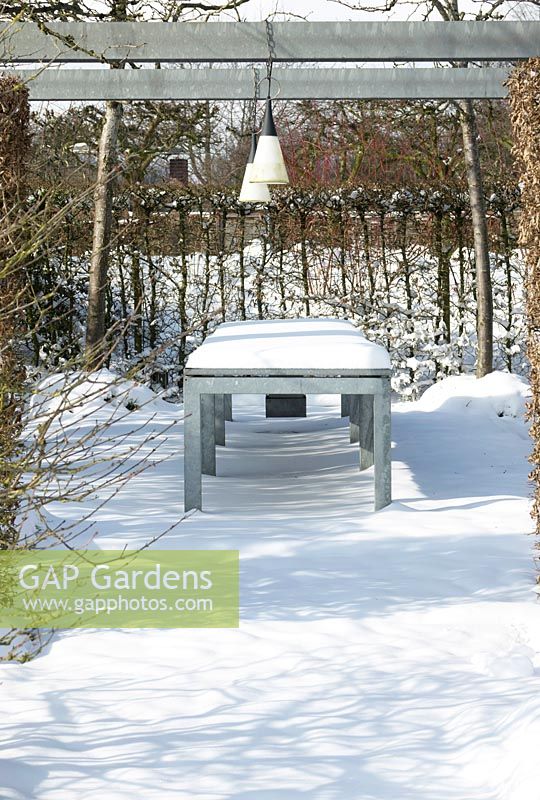 Terrasse avec table et lampes sous pergola recouverte de neige.