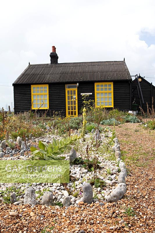 Cottage et jardin sur une plage de galets, parterre de pierres blanches avec des plantes