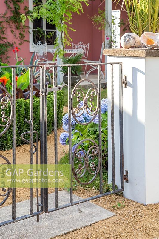 Vue à travers des portes métalliques au-delà des parterres vers la maison avec coin salon. Le rêve du jardin des Indianos - Hampton Court Flower Show 2019