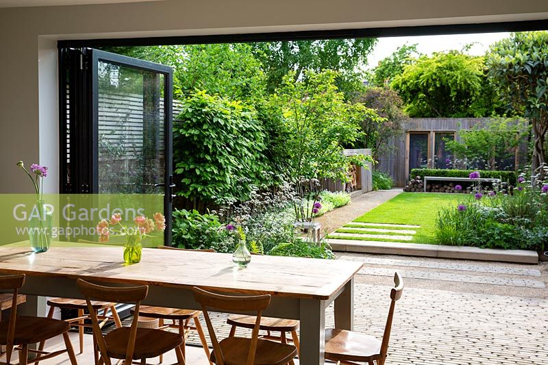Une salle à manger ensoleillée avec des portes vitrées ouvrant sur un jardin de ville contemporain.