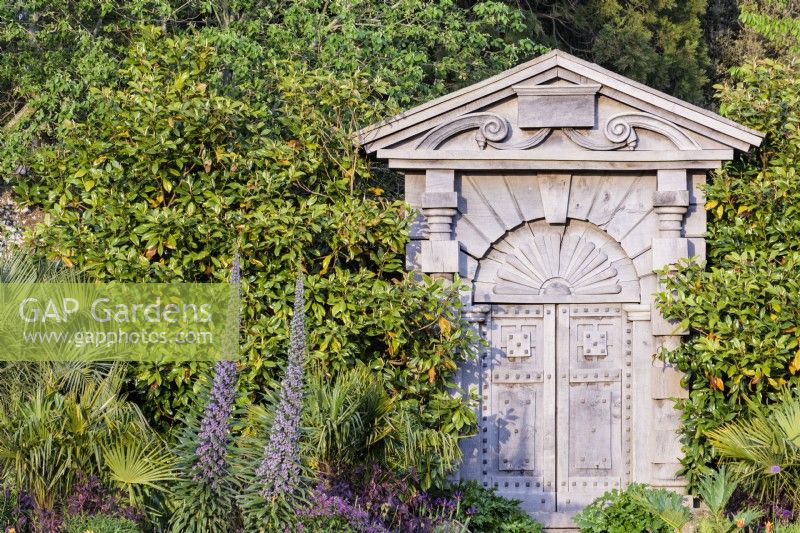 La porte italienne sculptée dans du chêne vert et basée sur les dessins d'Inigo Jones pour Arundel House à Londres du début du 17ème siècle dans le Collector Earl's Garden au château d'Arundel, West Sussex en mai. Encadré d'échiums et de palmiers.