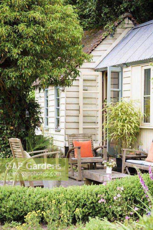 Studio de jardin d'architecte avec coin salon extérieur encadré de haies et de lierre taillé dans un jardin de cottage en juin