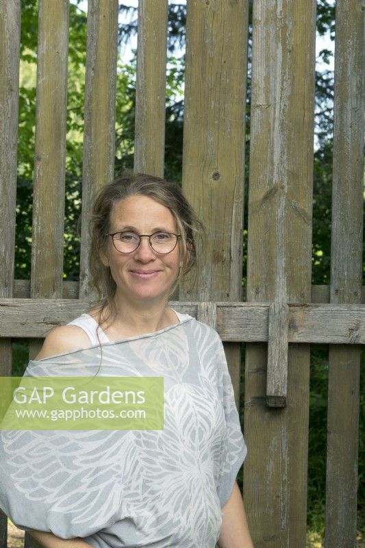 Femme debout près de la porte du jardin. Esther Kuiler propriétaire et conceptrice du jardin : de Ommuurde Tuin.