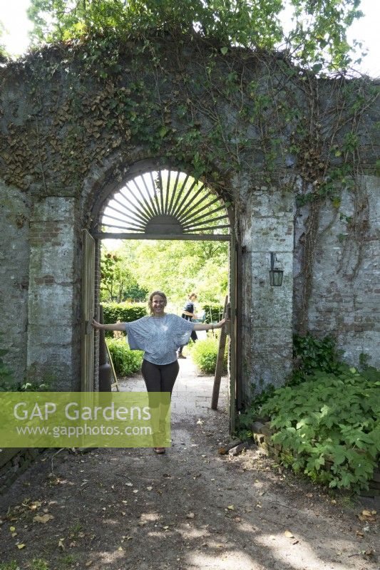 Femme debout près des portes du jardin. Esther Kuiler propriétaire et conceptrice du jardin : tuin de Ommuurde.
