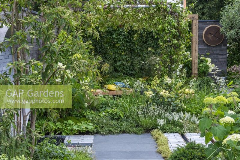 Un endroit pour se retrouver. Hampton Court Flower Festival 2021. Une cour urbaine est plantée dans des tons reposants de vert et de blanc, avec une hauteur ajoutée par une pergola drapée de jasmin étoilé.