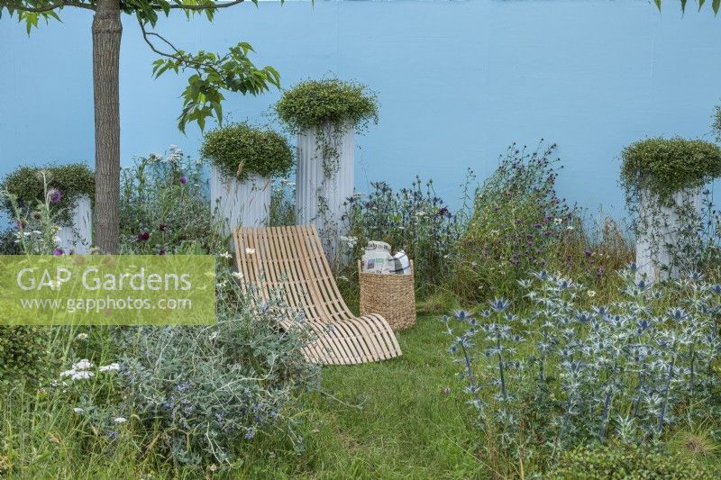 Jardin de la solitude. Une chaise longue est installée au milieu d'une plantation informelle de houx marins, de chardons, d'achillées et de scabieuses. De hautes jardinières en cascade avec des coussins laineux de Muehlenbeckia.