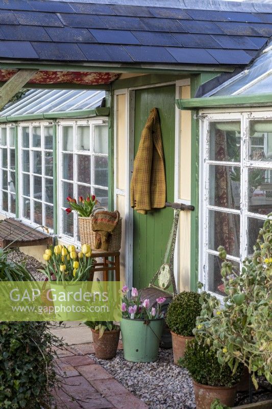 Porche et véranda peints en vert avec rouleau de jardin ancien et plantation de pots de printemps.