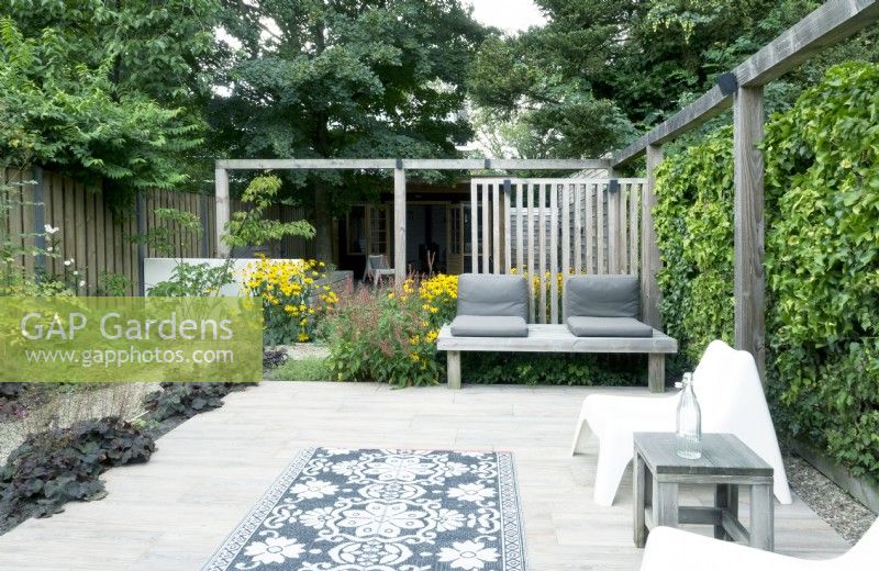 Terrasse avec pergola en bois, bancs en bois et tapis de jardin.