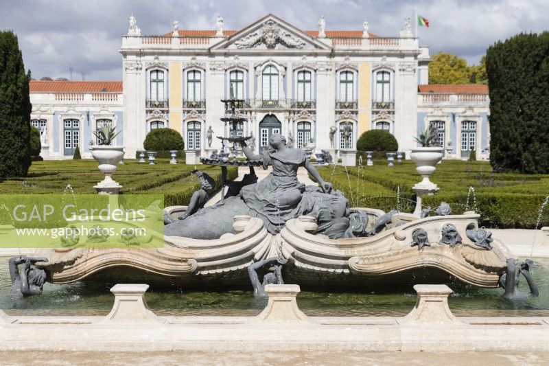 Fontaine ornée dans un étang surélevé montrant la sculpture, au-delà du parterre et du palais. Queluz, Lisbonne, Portugal, septembre.