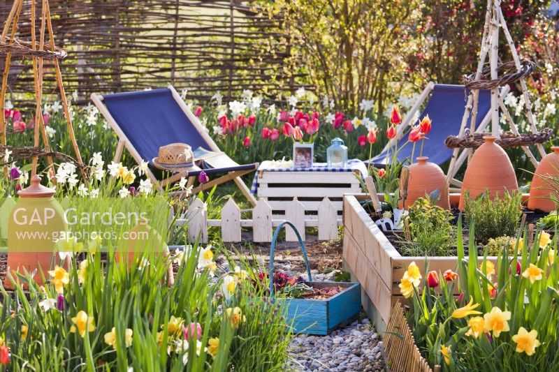 Parterres surélevés et parterres de tulipes et jonquilles en fleurs, ainsi que parterres de légumes. Coin salon à proximité avec transats.