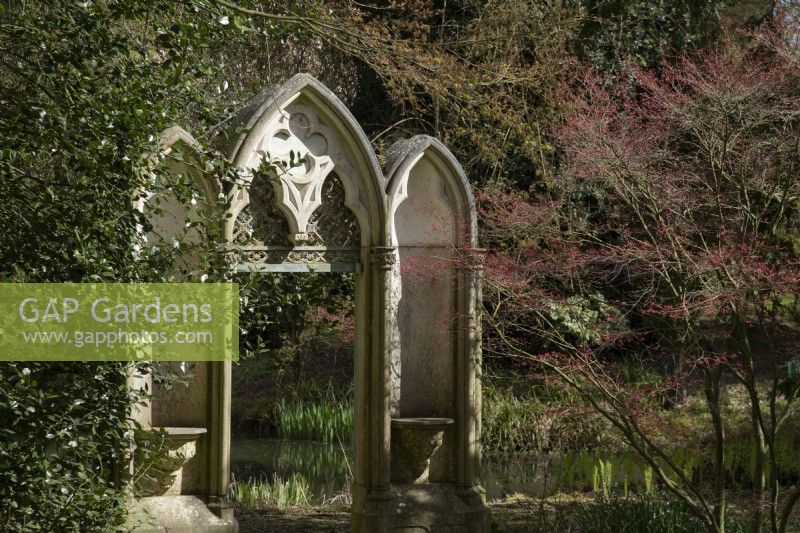 Une porte en pierre sculptée et un arbre Acer à côté du jardin d'eau à Thenford Gardens and Arboretum, Thenford, Banbury, Oxfordshire, UK