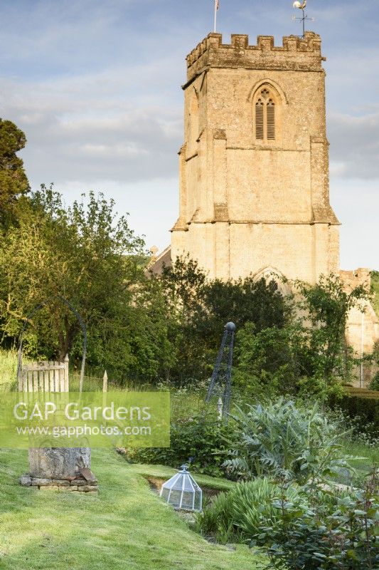 Jardin potager formel sur terrain en pente à l'ancien presbytère, Netherbury, Dorset en mai avec en toile de fond l'église St Mary
