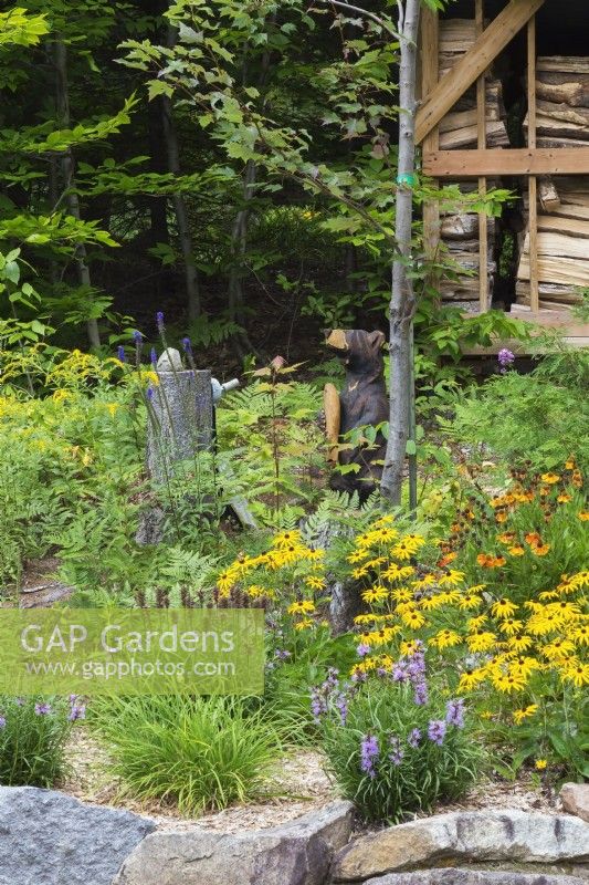 Jardin de devant au Québec avec sculpture d'ours dans un parterre de vivaces à fleurs - août