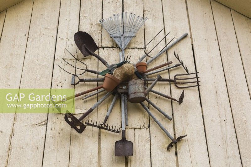 Vieux outils de ferme et de jardin accrochés au mur blanc de la grange dans le jardin de campagne de l'arrière-cour, Québec, Canada - août