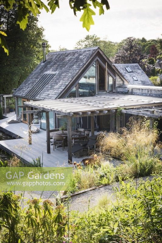 Maison conçue par Hugh Wray-McCann à Am Brook Meadow dans le Devon en juin, où une terrasse en bois le long d'un côté du bâtiment est recouverte d'un toit ouvrant en bois.