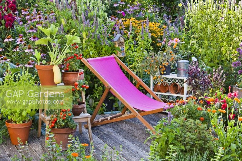 Patio en terrasse avec chaise et pot cultivant des légumes et des herbes bordés d'un parterre de fleurs herbacées avec Agastache et Echinacea.