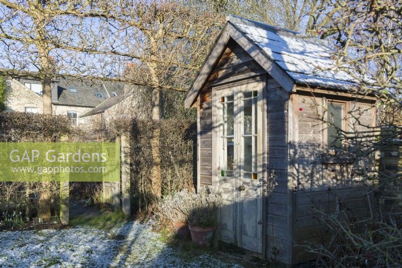 Petite maison d'été de jardin en bois fabriquée à partir d'un abri de jardin restylé à côté d'une haie d'aubépines et d'érables des champs plissés. janvier