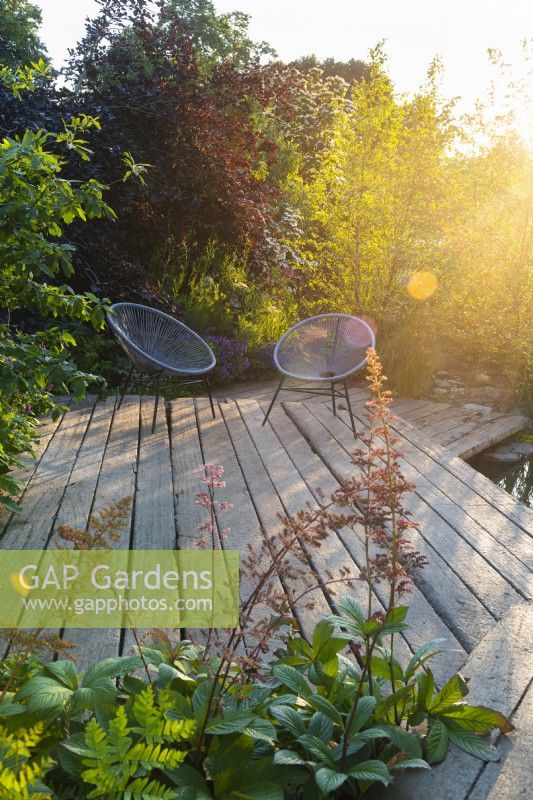 Terrasse en bois en bois avec deux chaises au coucher du soleil. RHS Garden pour un avenir vert. Conçu par Jamie Butterworth. RHS Hampton Court Palace Garden Festival Show, juillet 2021