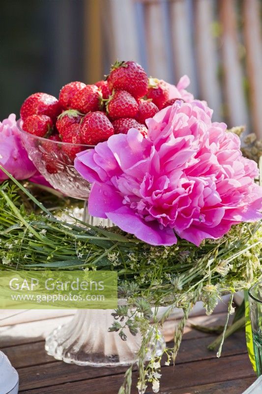 Présentoir à gâteaux avec couronne de fleurs sauvages, pivoines et fraises.
