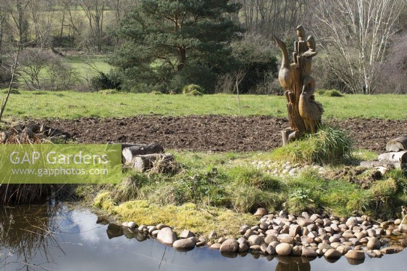 Statue d'oiseau sculpté en bois à côté de l'étang de la faune dans John's Garden à Ashwood Nurseries - Kingswinford - Spring