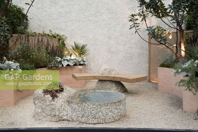 Cour de jardin en pot d'inspiration méditerranéenne avec parterres de fleurs surélevés incurvés, banc en pierre et pièce d'eau.