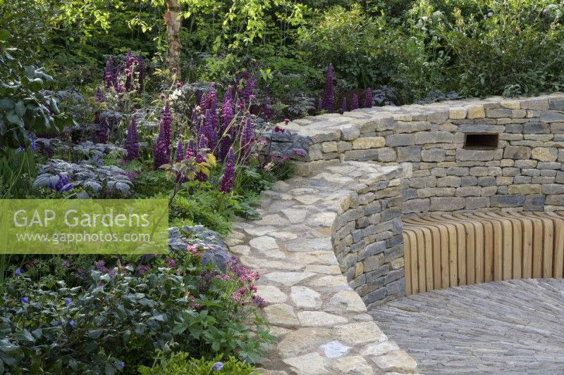 Mur en spirale en pierre avec banc en bois intégré et plantation de lupins - The RAF Benevolent Fund Garden