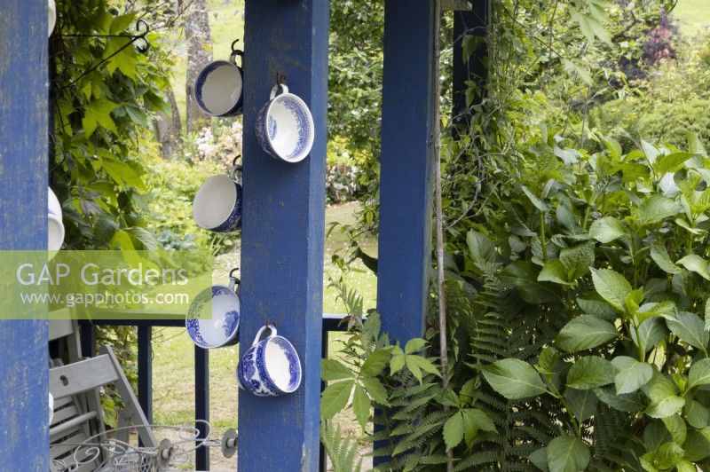 De vieilles tasses à thé sont réutilisées dans des décorations sur un hangar en bois bleu. Lewis Cottage, jardin NGS Devon. Le printemps.