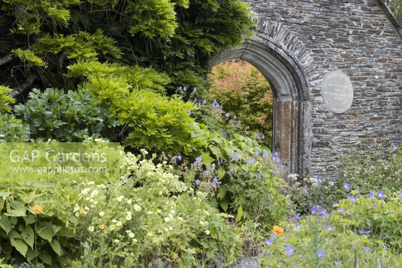 Vue sur l'arche orientale avec divers feuillages et fleurs au premier plan. La maison du jardin, Yelverton, Devon. Été.