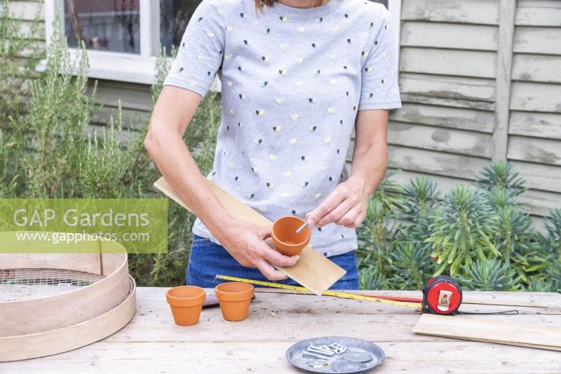 Femme fixant les pots à la planche en bois à l'aide de rondelles, d'écrous à oreilles et de boulons