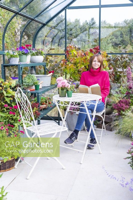 Femme assise à une table lisant dans une serre qui a été remplie de diverses plantes et pots mélangés