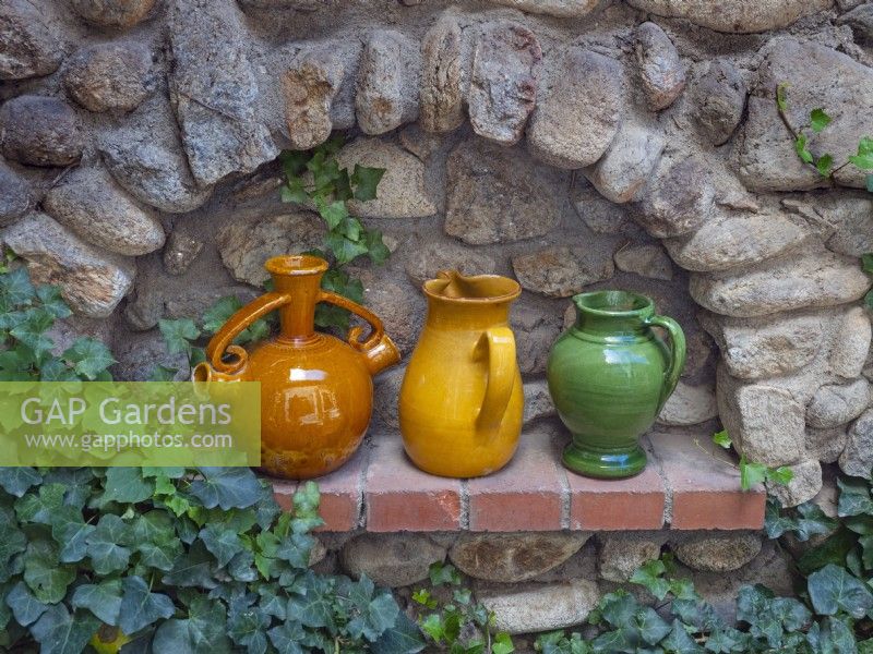 Des cruches de vin en poterie décorent une alcôve dans un mur de jardin en pierre