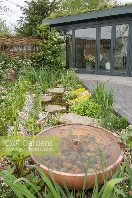 Terrasse en bois menant à un bureau à domicile, à côté d'une pièce d'eau en cuivre et d'une plantation de gravier - The Hide Garden, RHS Malvern Spring Festival 2022