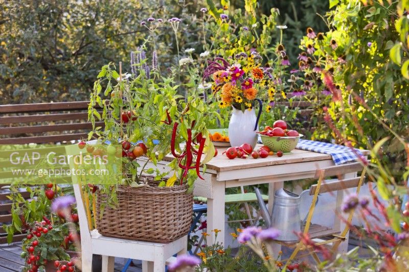 Bouquet de fleurs sur table et légumes en pot sur terrasse aménagée avec salon de jardin.